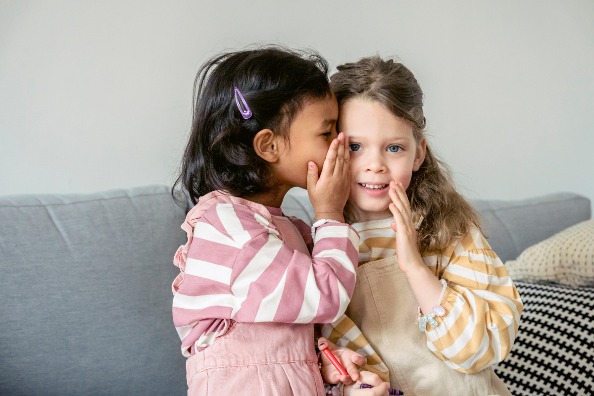 Hispanic girl whispering secret on ear of friend